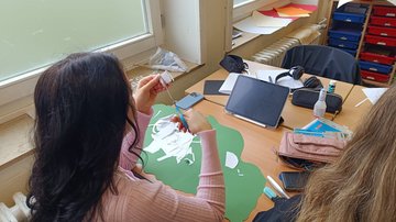 Eine Schülerin schneidet etwas aus um ein Ausstellungsplakat zu gestalten