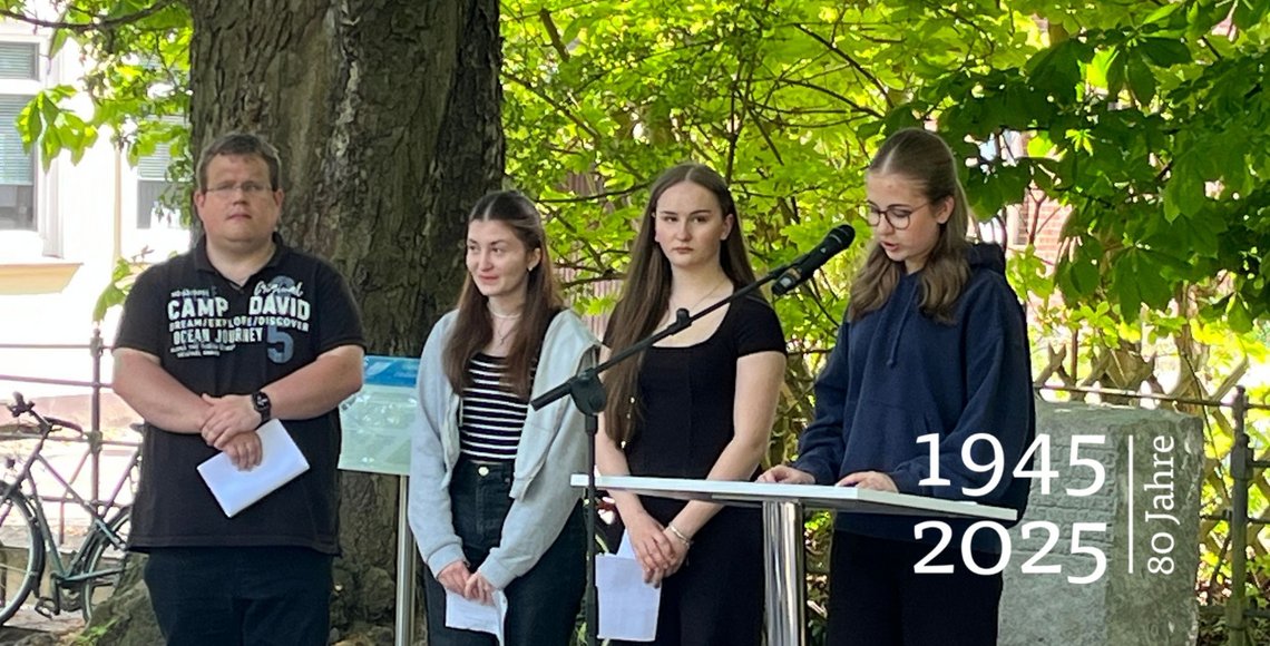 Drei Schülerinnen und ihr Lehrer. Eine der Jugendlichen spricht in ein Mikrofon.